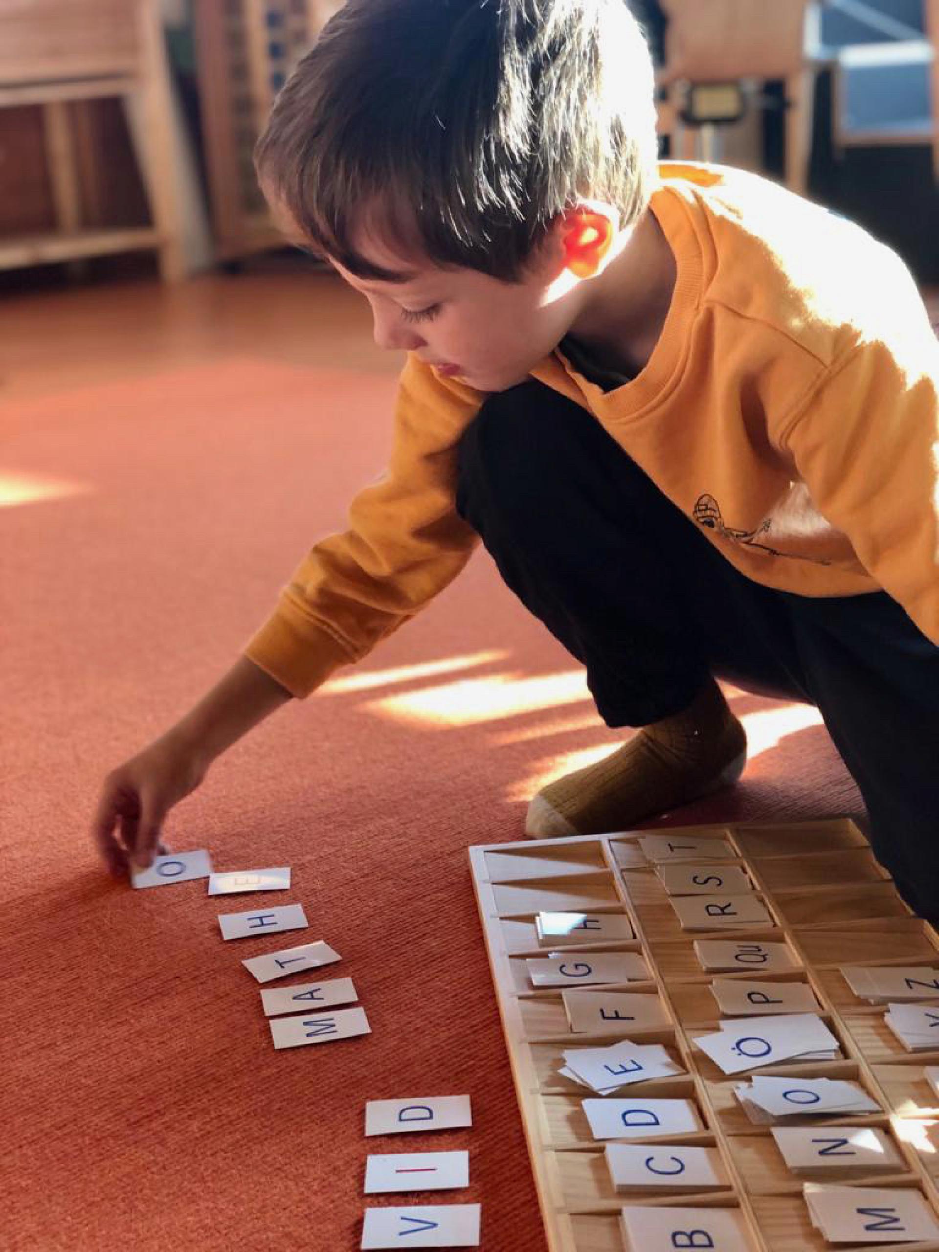 A young boy plays with a wooden board with letters on it